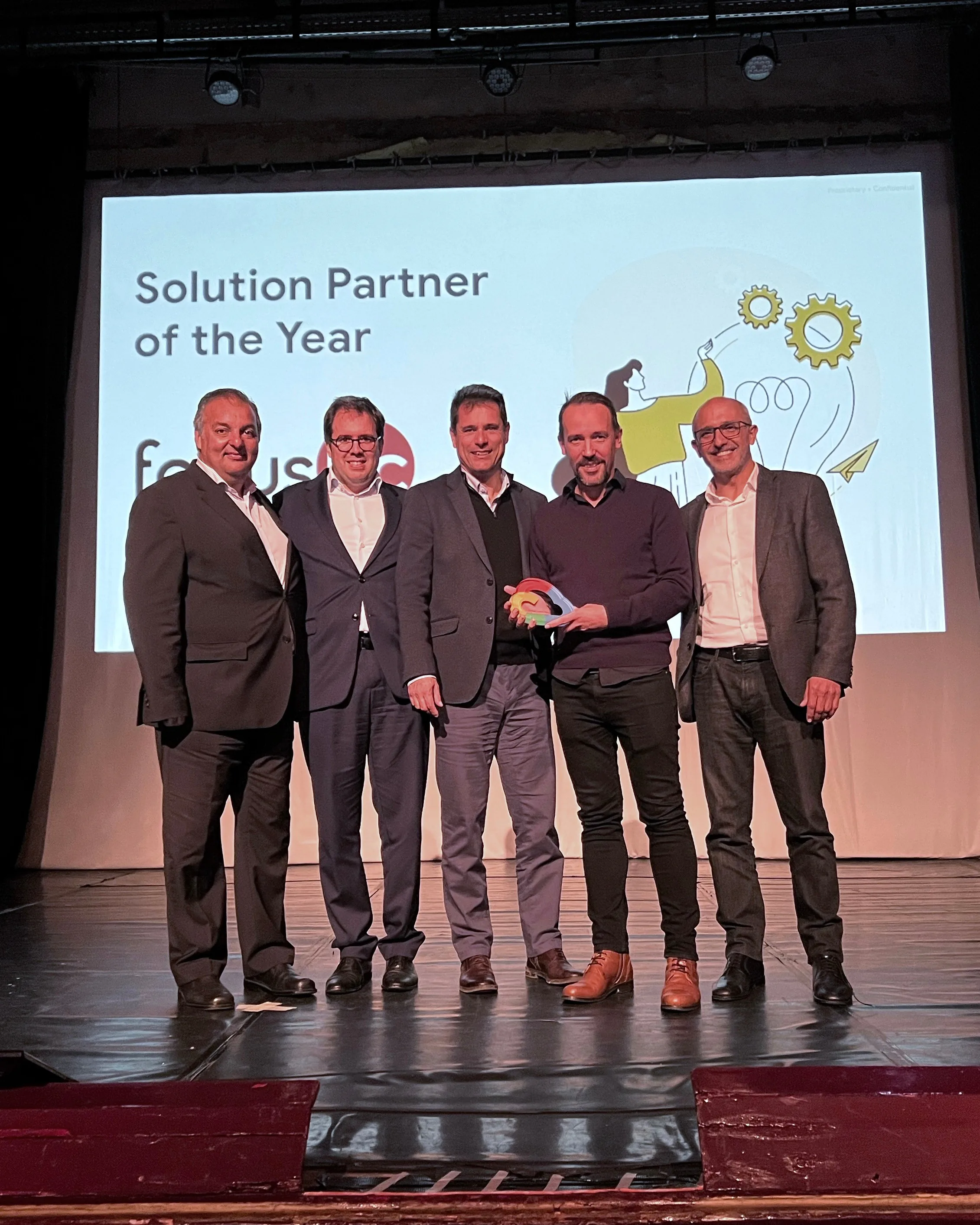 Colorful neon light shaped like the Focus BC logo placed on a pedestal indoors, glowing in blue, yellow, and pink tones.