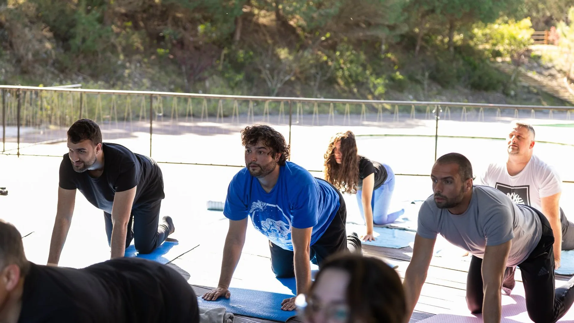 Two men standing at the front of the room during a presentation, one speaking while the other listens beside a laptop on a table.