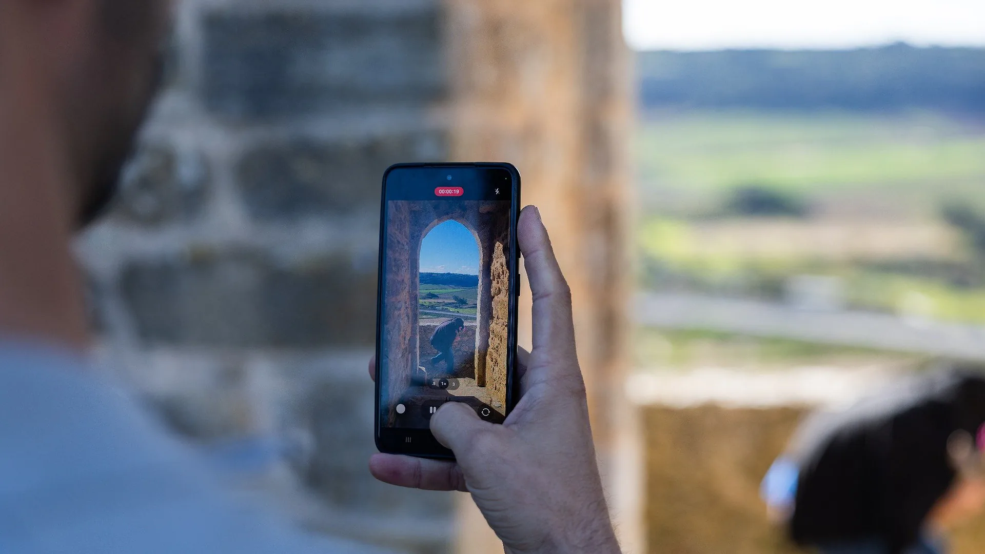 Two men looking down at a phone while others stand nearby, appearing to choose a song during karaoke night.
