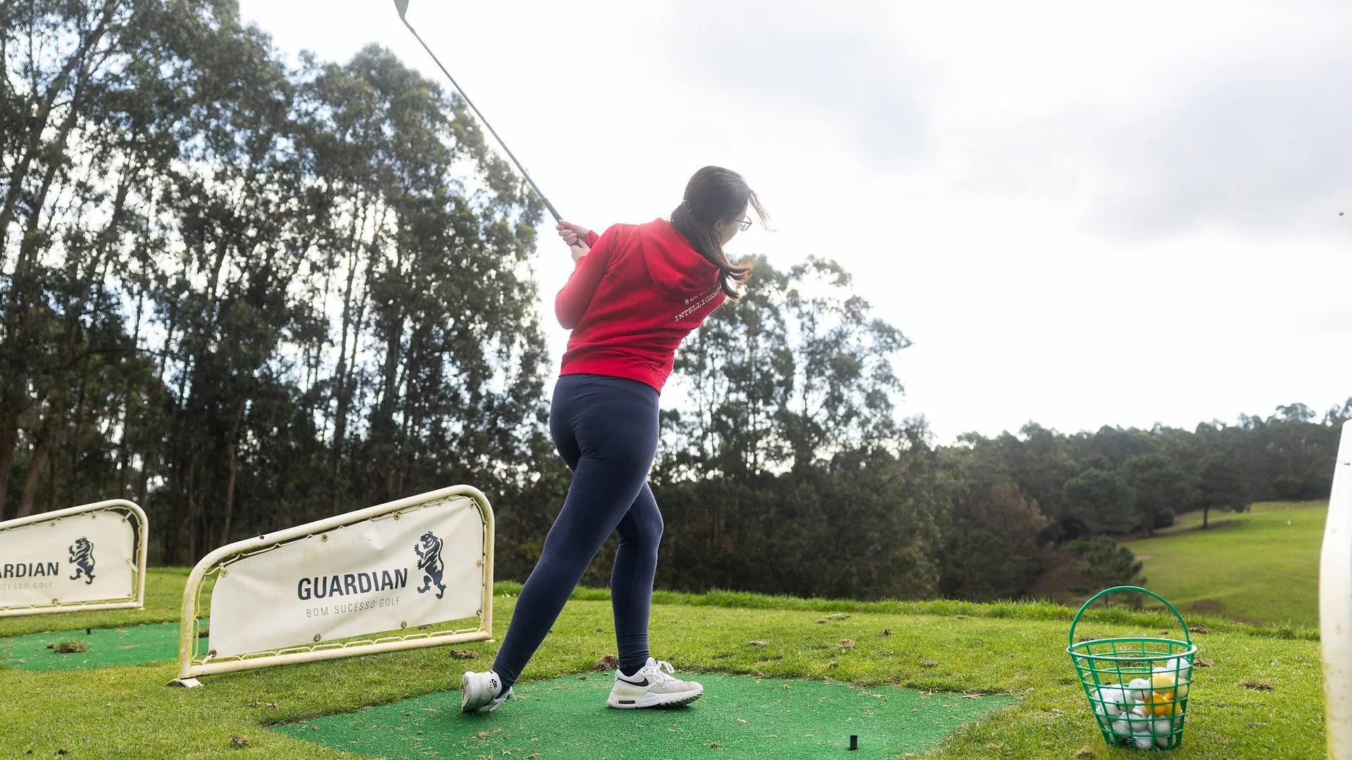 Man in a red jacket singing energetically into a microphone under colorful party lights, with colleagues watching during karaoke night.
