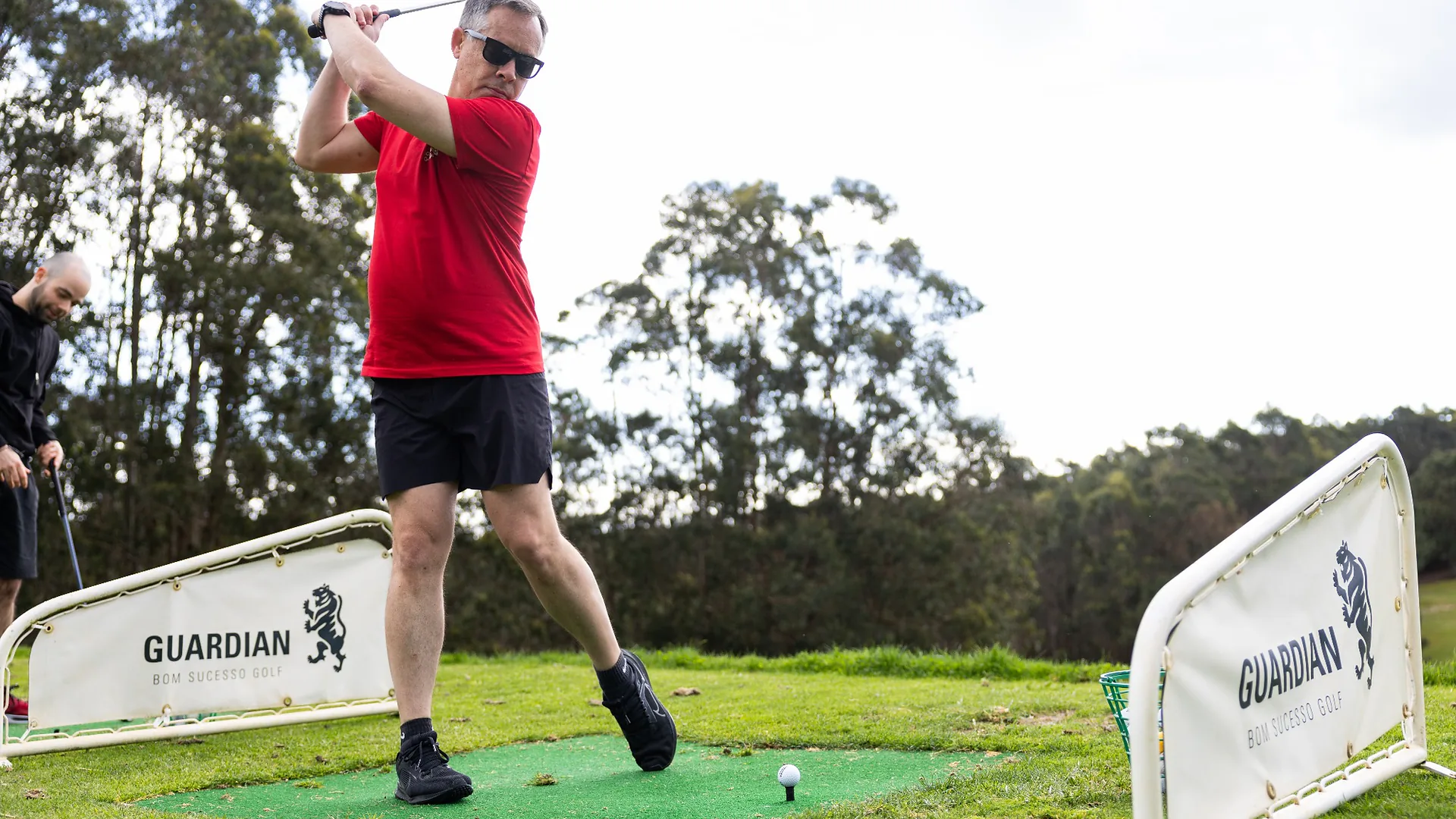 Woman standing with arms crossed listening to a colleague in a red hoodie during an outdoor yoga session introduction.