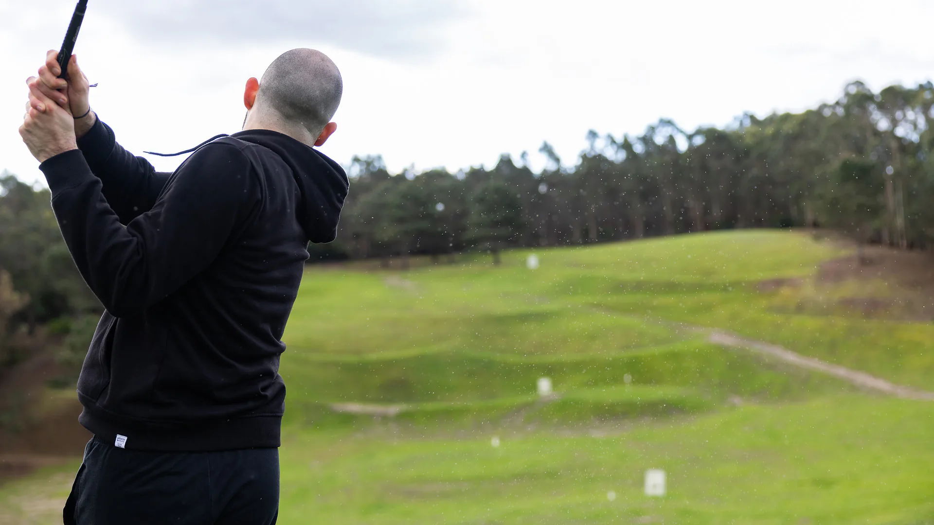 Woman standing with arms crossed listening to a colleague in a red hoodie during an outdoor yoga session introduction.